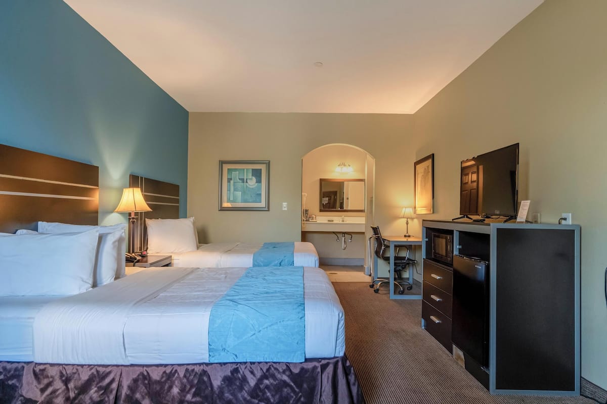 A hotel room with two beds, a desk, a dresser, a mirror, and a television.