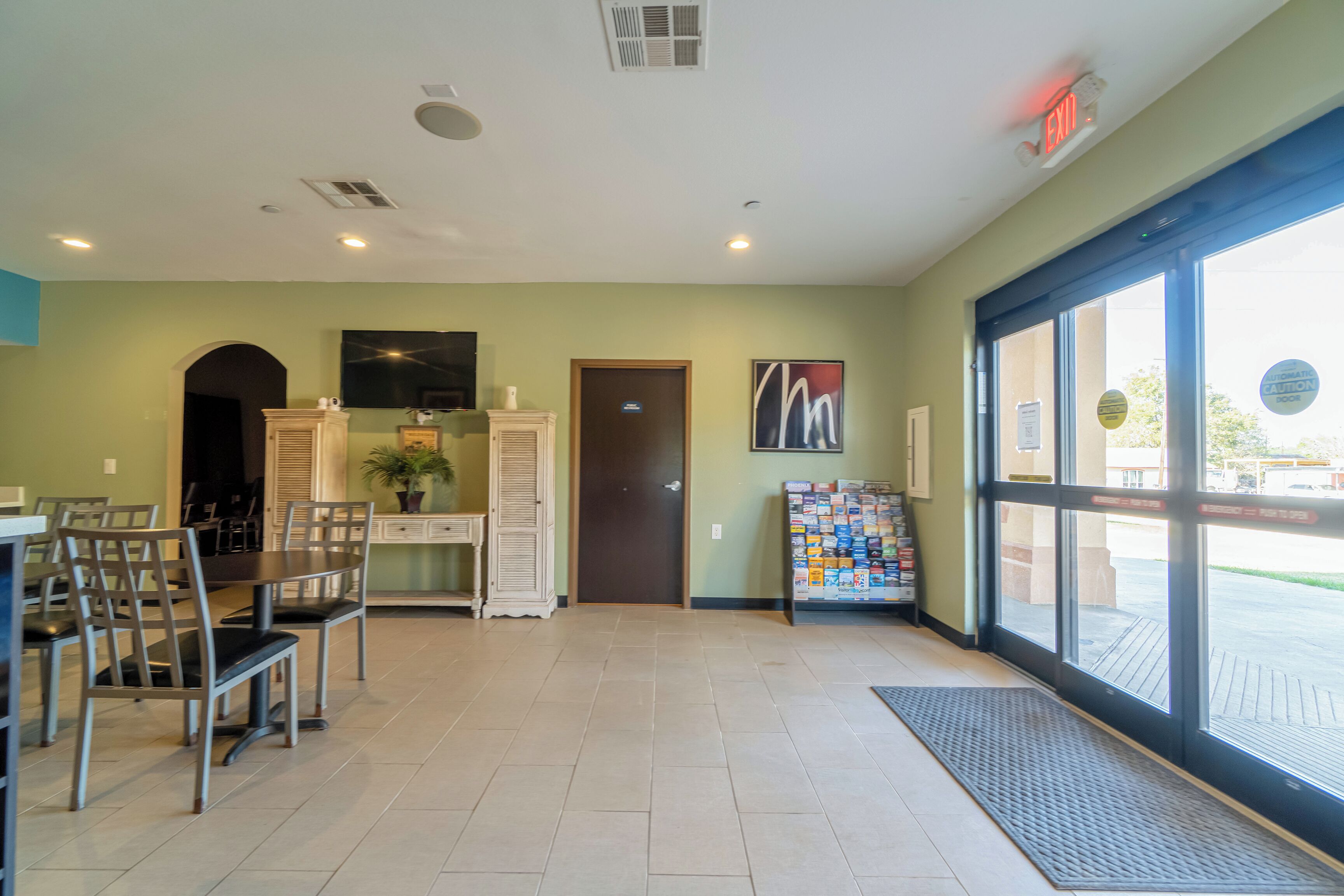 A spacious indoor area with a dining table and chairs, a reception desk, a door, and a large window.