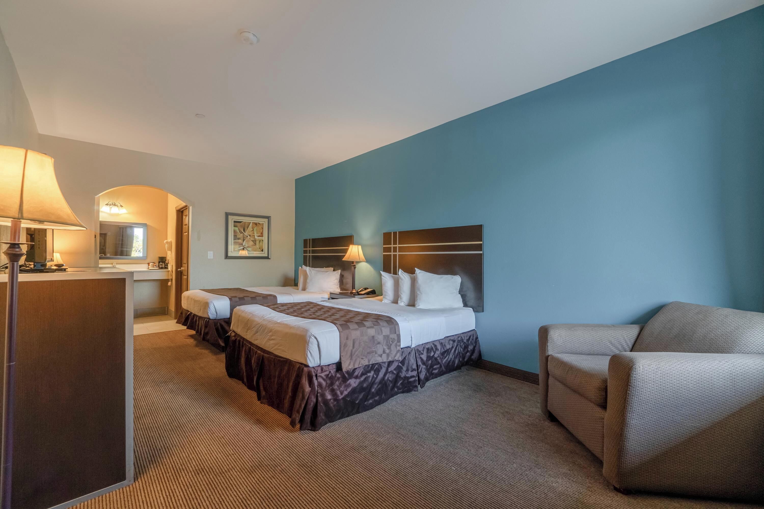 Habitación de hotel con dos camas, un escritorio, una silla y un ventanal grande.