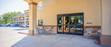 A hotel entrance with a stone facade, a glass door, and a parking lot visible in the background.