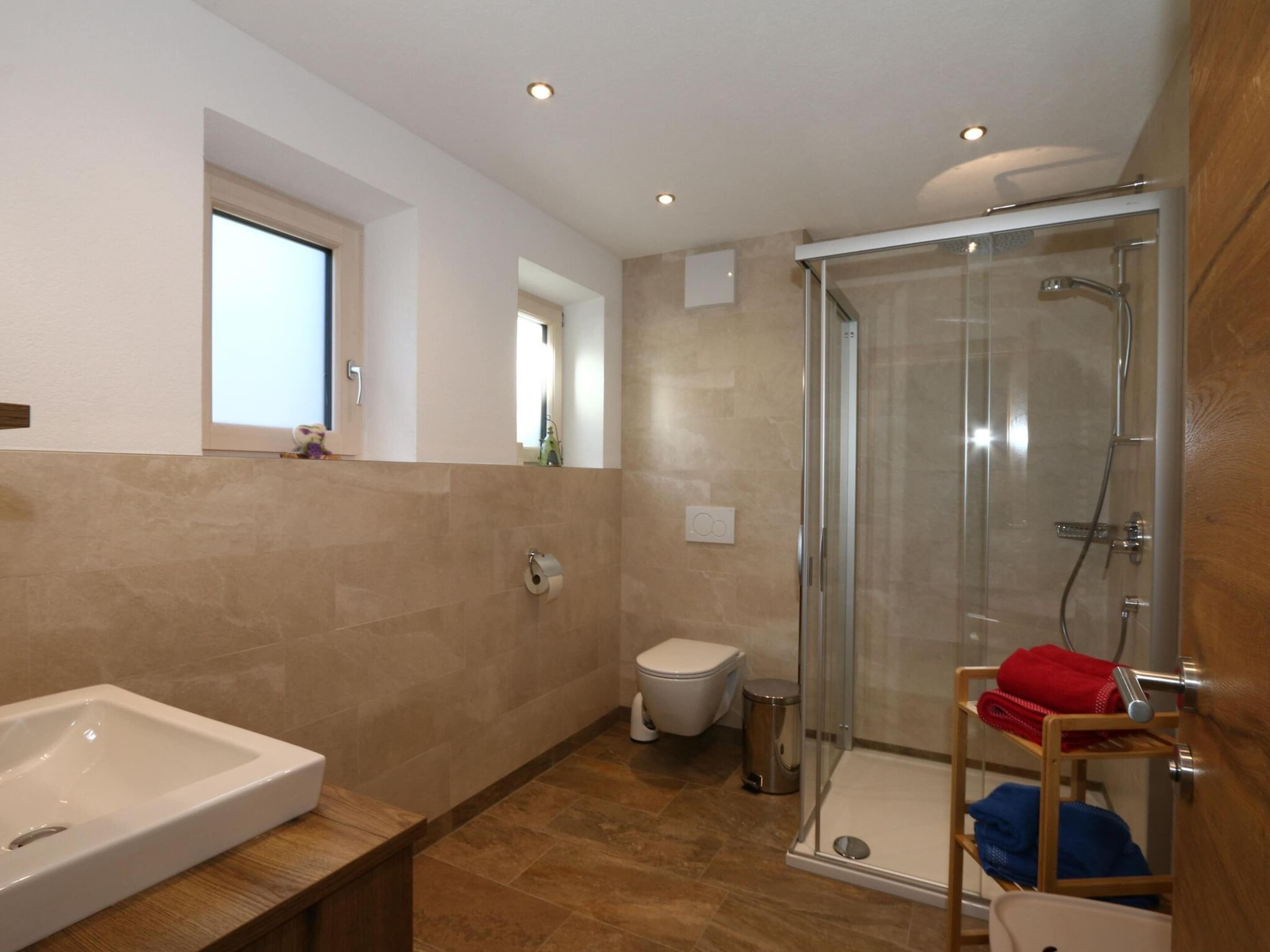 A modern bathroom with a glass shower enclosure, a white toilet, and a wooden vanity with a sink.