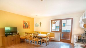 A dining area with a wooden table and chairs, a television on a cabinet, and a window with a view of buildings. - Apartment Neustift Near Stubai Ski Lift (Neustift Im Stubaital)