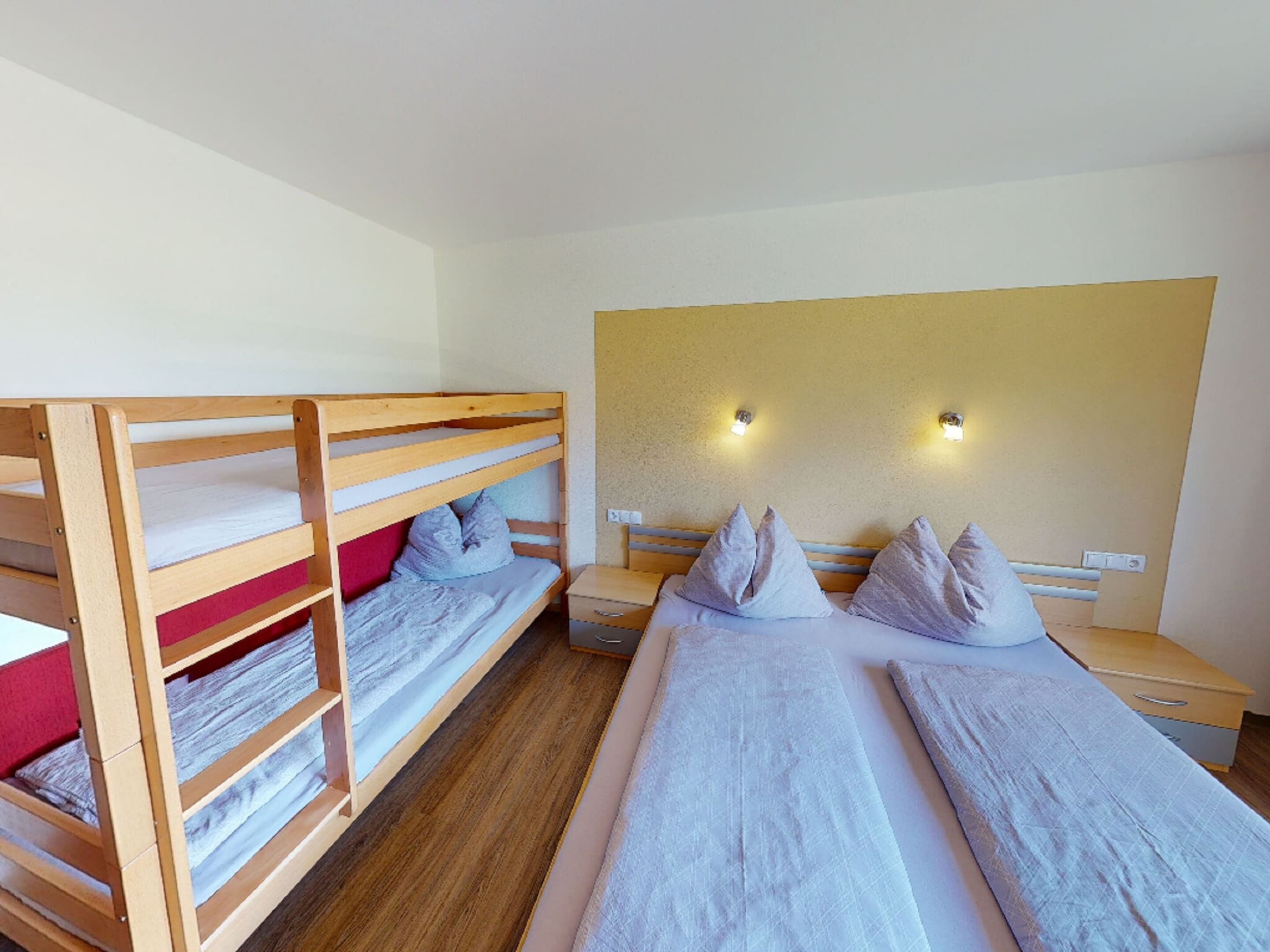 A room with bunk beds, a large bed, and two bedside tables with lamps.
