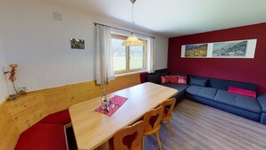 Ein Essbereich mit Holztisch und Stühlen, einem Fenster mit Vorhängen, einer roten Wand mit Bildern und einem blauen Sofa.