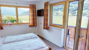 Ein Schlafzimmer mit Bett, Fernseher und einem Balkon mit Blick ins Grüne.