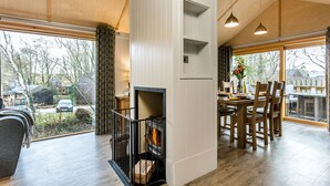 A modern interior with a fireplace, dining area, and large windows offering views of the outside. - Lodge 16 (Wareham)