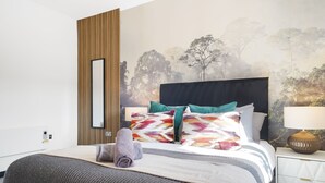 A neatly made bed with a patterned pillow set, a rolled towel, and a bedside table with a lamp.