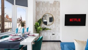 A modern living room with a dining area, a large mirror, and a TV displaying "NETFLIX".