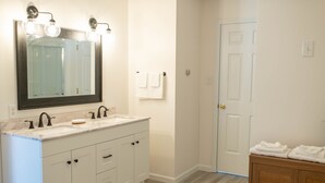 A bathroom with a double sink vanity, a large mirror, and a wooden cabinet with towels.