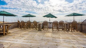 Terraza de madera con mobiliario exterior y sombrillas, con vista a una playa.