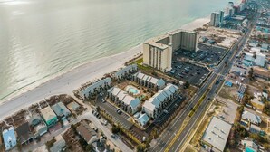 Vista aérea de un hotel costero con varias construcciones, un estacionamiento y una playa al fondo.
