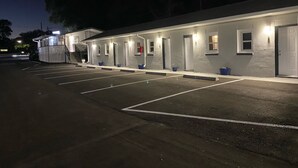 Ein Motel mit einer Reihe von Zimmern, jedes mit einer Tür und einem Fenster. Vor dem Motel befindet sich ein Parkplatz.