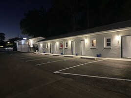 Un motel avec une rangée de chambres, chacune dotée d’une porte et d’une fenêtre. Un parking se trouve devant le motel.