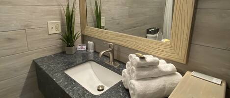 A bathroom with a granite countertop, a sink, a mirror, a towel rack, and a wooden vanity.