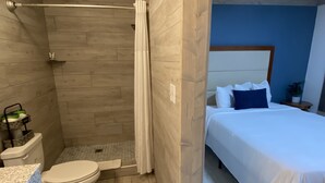 Ein Badezimmer mit Dusche, Toilette und Waschbecken sowie ein Schlafzimmer mit Bett und Nachttisch.