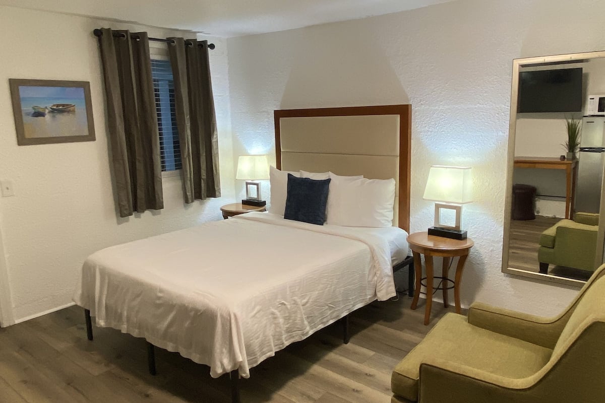 Ein Hotelzimmer mit Bett, Sessel, Nachttisch, Lampe, einem Bild an der Wand und einer Deckenleuchte.