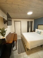A bedroom with a bed, a desk, a chair, a TV mounted on the wall, and a door.
