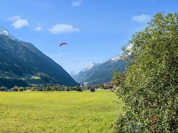 Paesaggio montuoso con cielo sereno, un prato erboso e un edificio all'orizzonte.