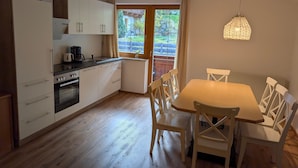 A modern kitchen with white cabinets, a black countertop, and a dining area with a wooden table and white chairs. - Apartment Neustift Near Stubai Ski Lift (Neustift Im Stubaital)