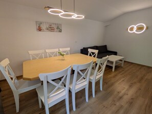 Un comedor con mesa de madera y sillas blancas, un sofá negro y un cuadro en la pared.