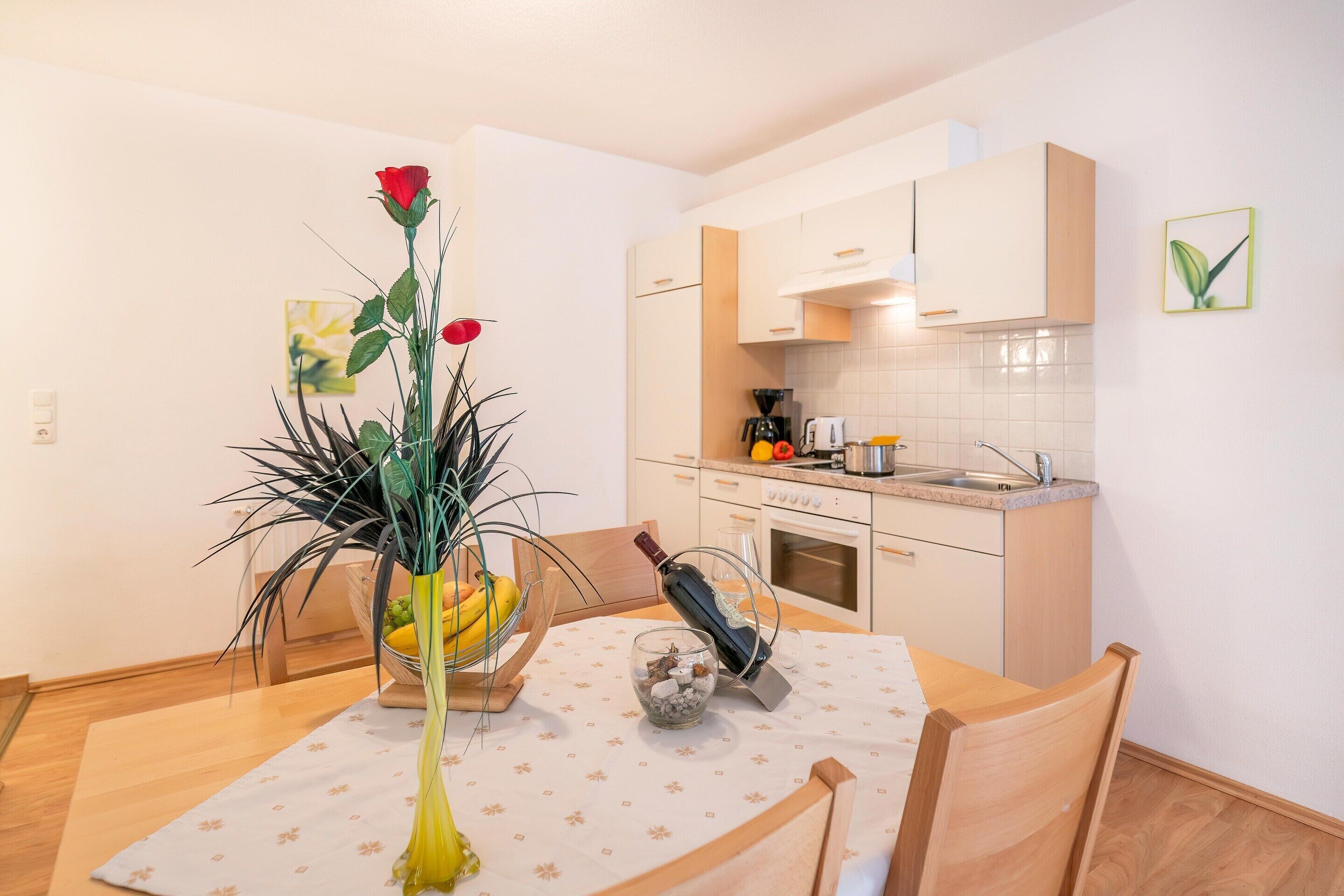 A dining table with a vase of flowers, a bowl of fruit, and a wine bottle.