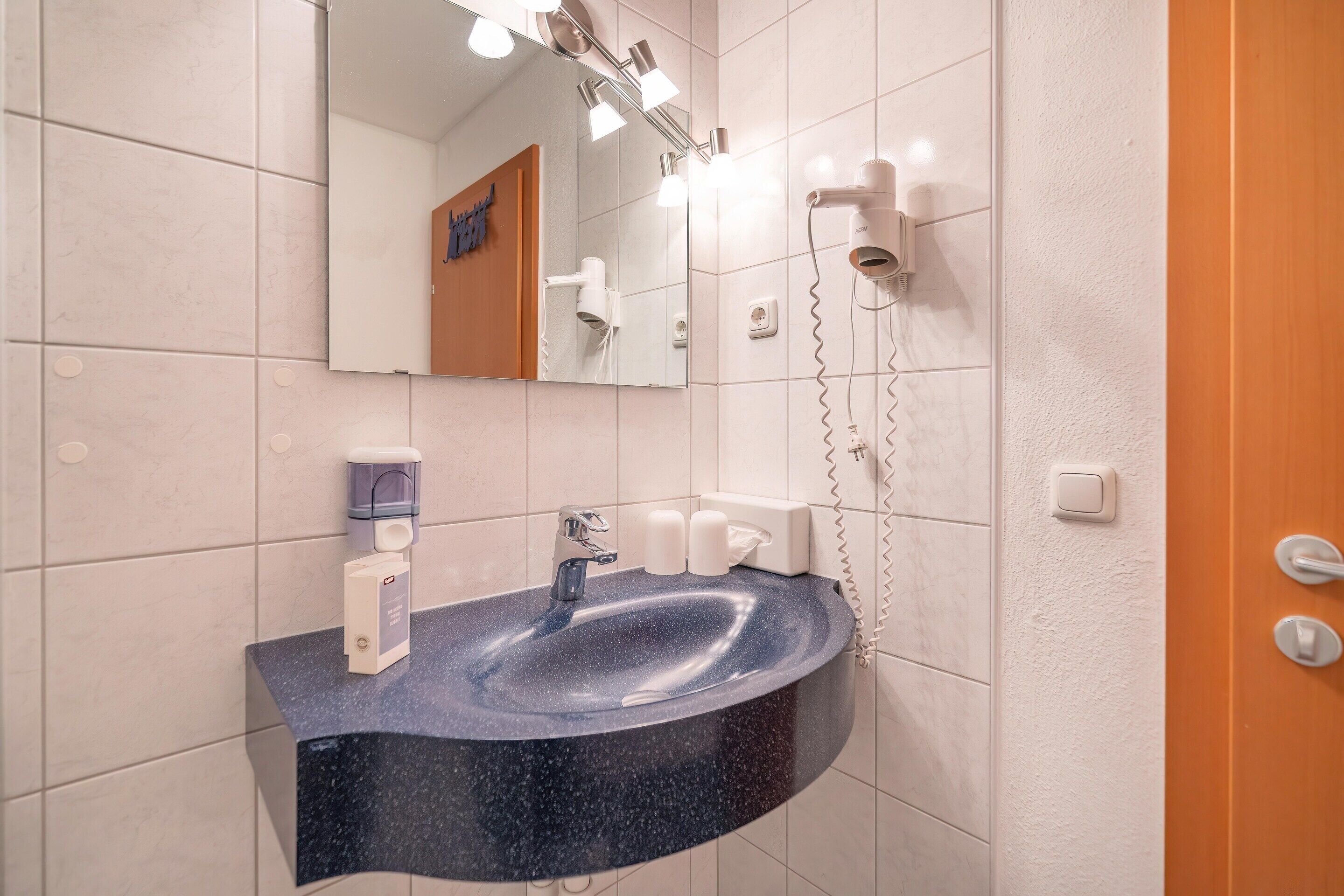 A bathroom with a dark blue sink, a mirror, and a hairdryer mounted on the wall.