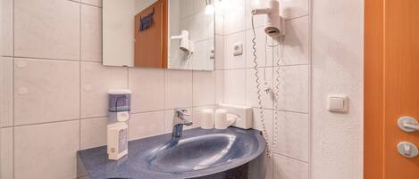 A bathroom with a dark blue sink, a mirror, and a hairdryer mounted on the wall.