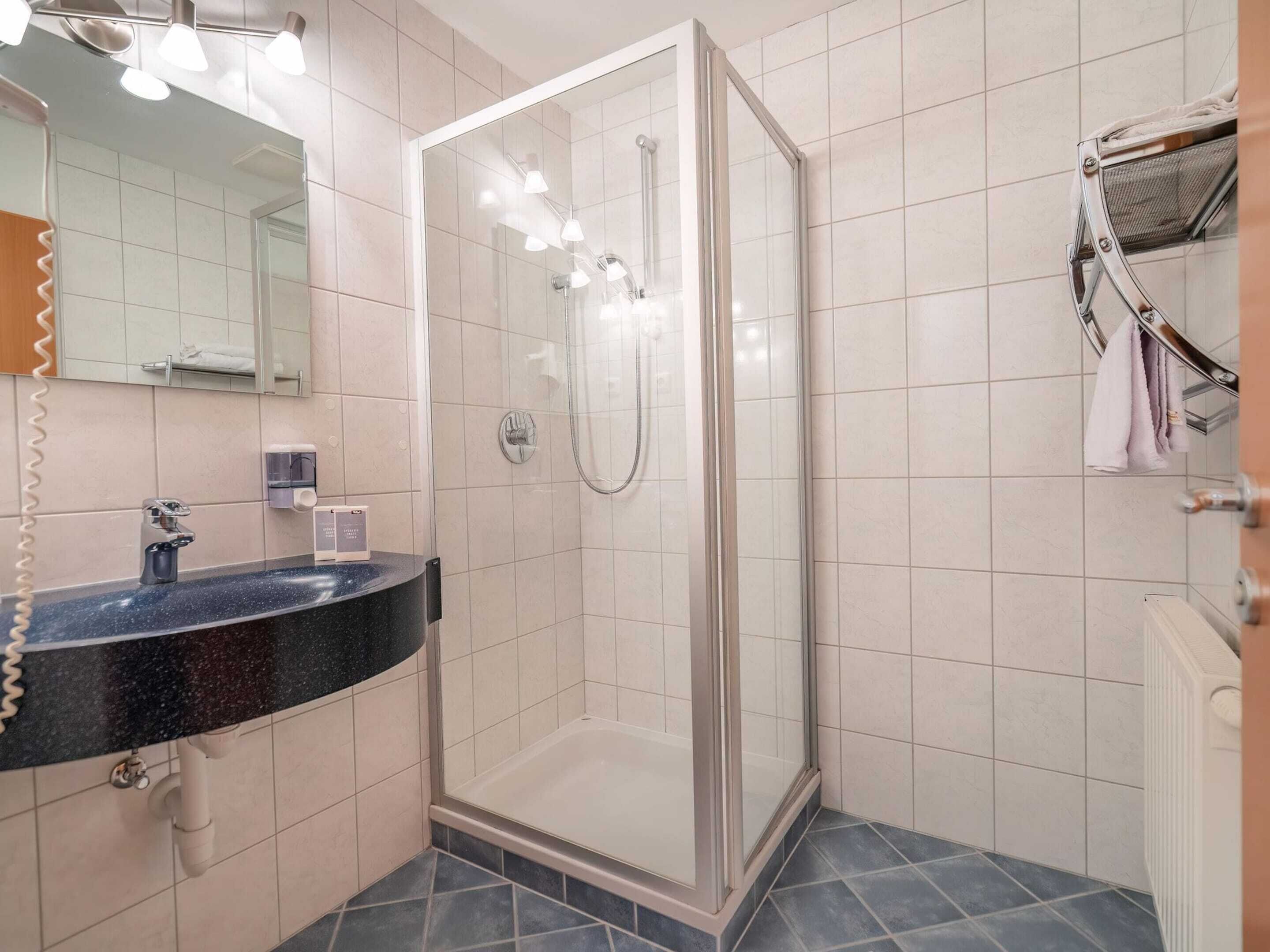 Une salle de bain moderne avec une douche à parois de verre, un lavabo noir avec un miroir au-dessus et un porte-serviettes avec des serviettes.