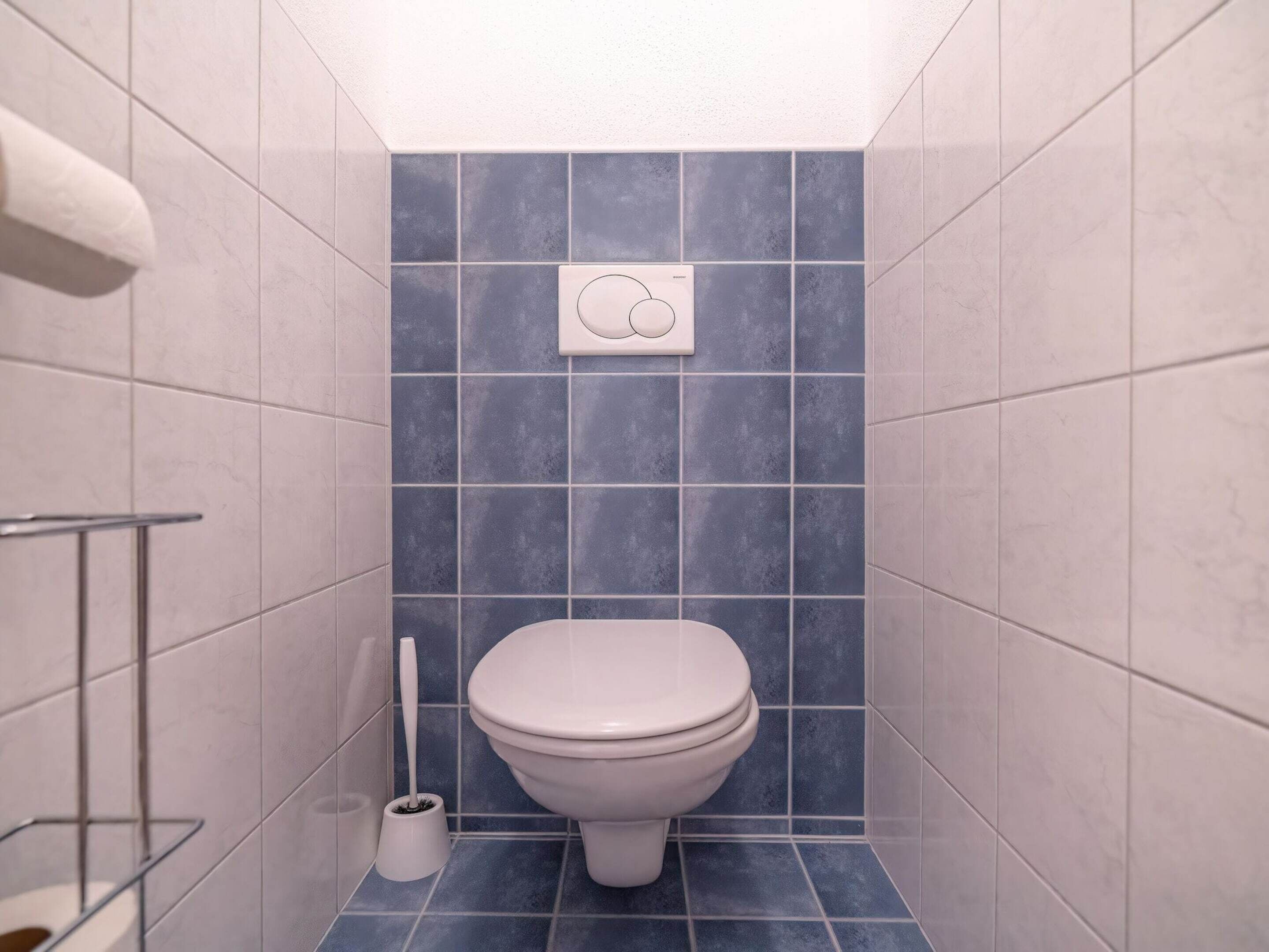 Une petite salle de bain équipée de toilettes, d’un sèche-mains et d’une brosse pour les toilettes.