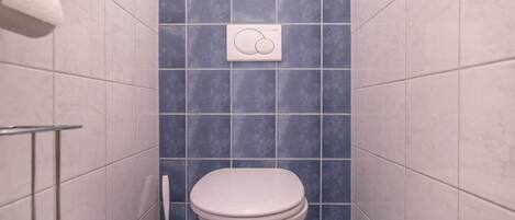 Une petite salle de bain équipée de toilettes, d’un sèche-mains et d’une brosse pour les toilettes.