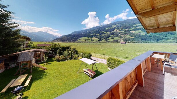A wooden deck with a view of a green field and mountains.