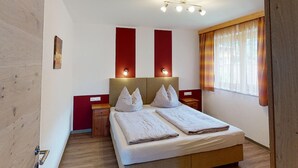 A hotel room with a large bed, two bedside tables, a nightstand, a wall-mounted light, and a window with curtains.