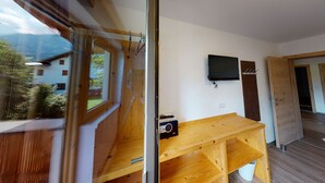 A room with a wooden desk, a mounted television, and a window overlooking a mountain.