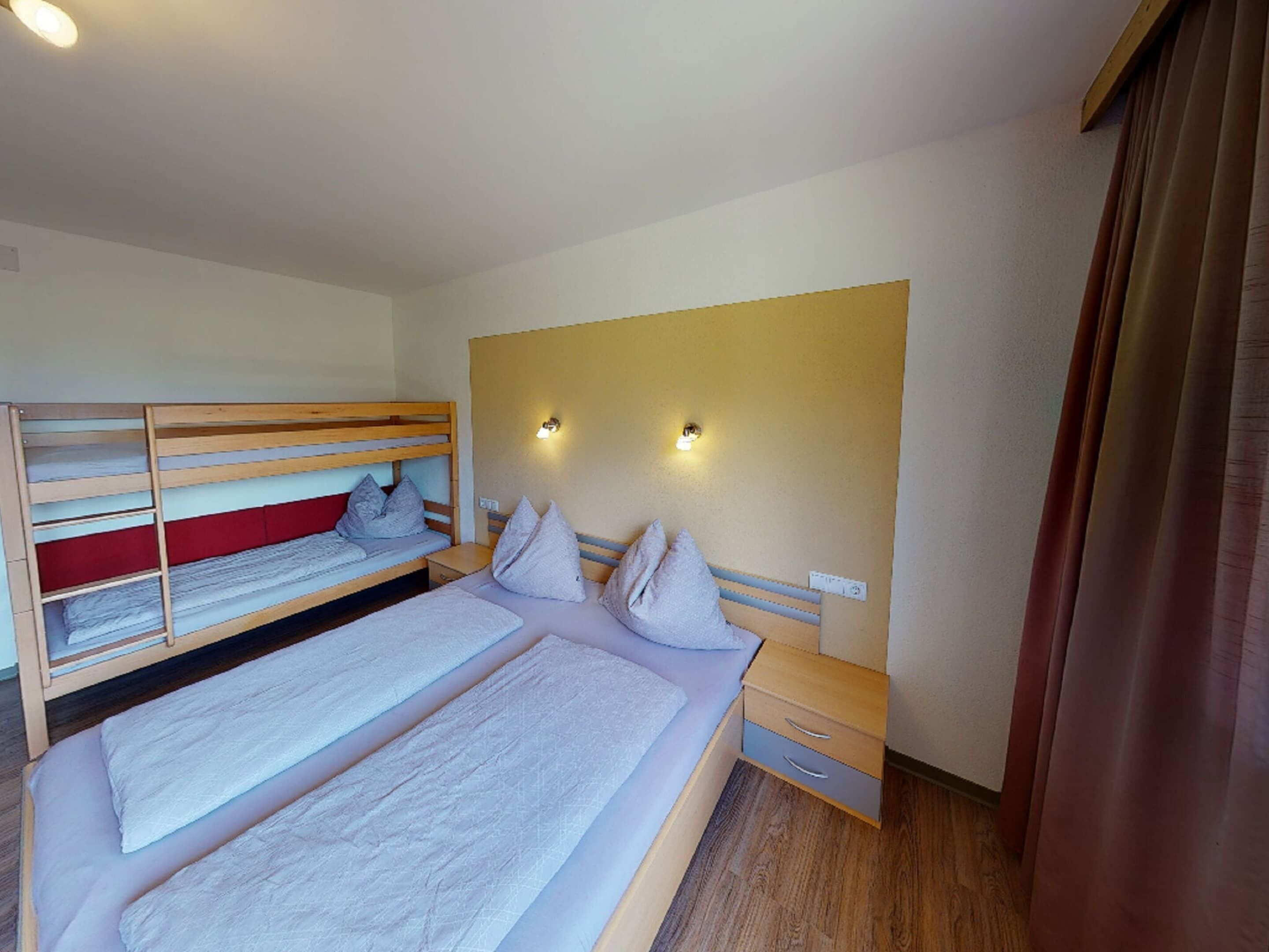 Une chambre avec des lits superposés, une table de chevet, une commode et une tête de lit dotée de lampes fixées au mur.