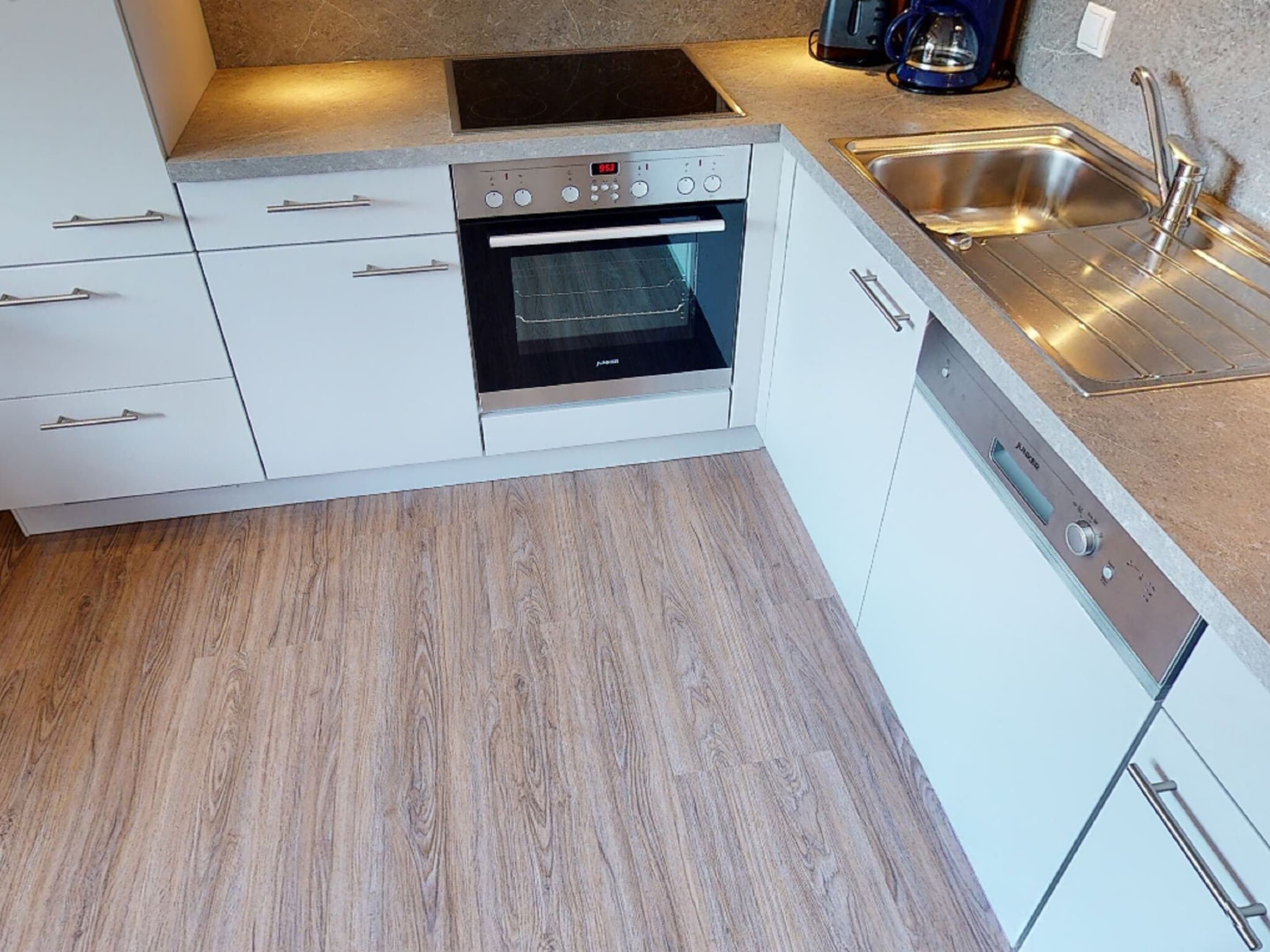 Eine moderne Küche mit weißen Schränken, einem eingebauten Ofen, einer Edelstahl-Spüle und einer Kaffeemaschine.