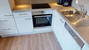 A modern kitchen with white cabinets, a built-in oven, a stainless steel sink, and a coffee maker.