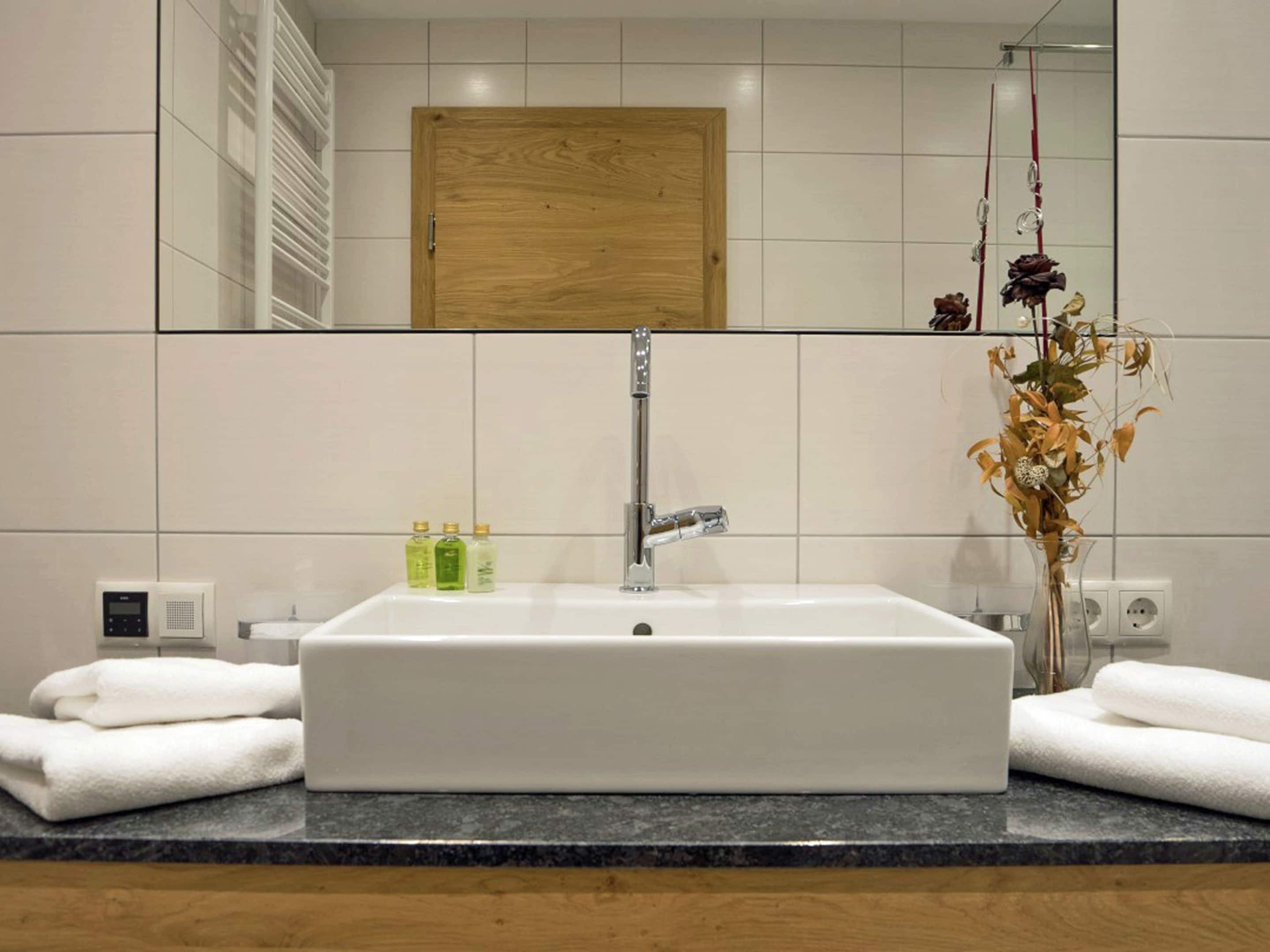 Un baño con un espejo grande, un lavamanos rectangular y una puerta de madera.