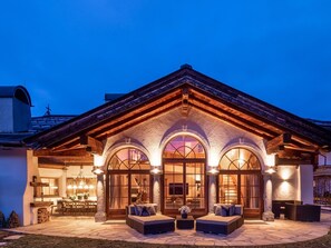 A large, well-lit building with a stone facade, multiple arched windows, and a spacious outdoor seating area with sofas and tables. - Exclusive Tyrolean Chalet Near Ski Lifts (Sankt Johann in Tirol)
