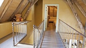 Una escalera estrecha con barandilla de madera que sube a una zona superior con un osito de peluche.