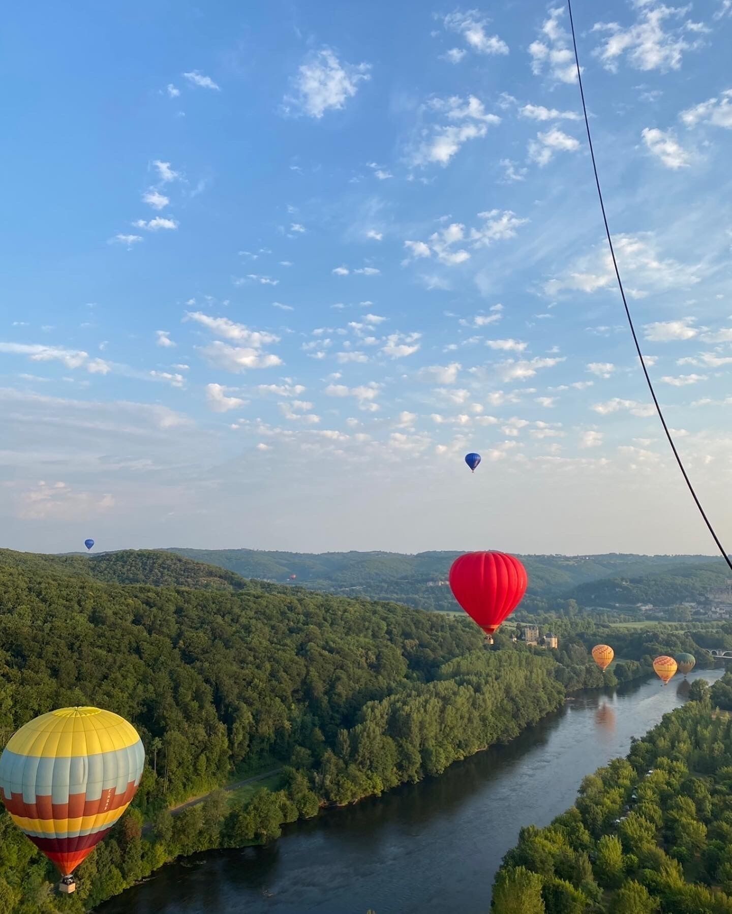A river with hot air balloons in the distance, surrounded by lush greenery.