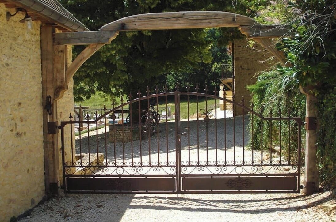 A gated entrance with a wrought iron gate, a stone wall, and a paved path leading to a building.