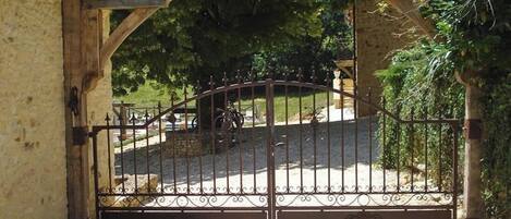 A gated entrance with a wrought iron gate, a stone wall, and a paved path leading to a building.