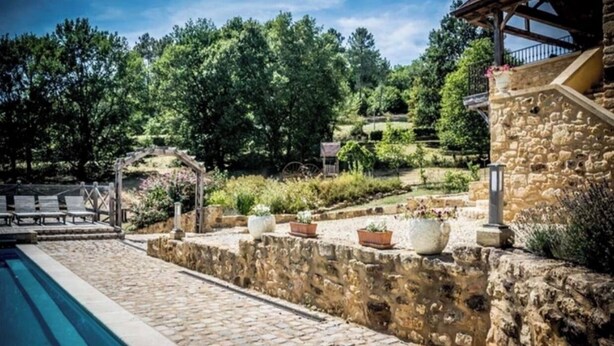 Una piscina de piedra con cubierta de madera, rodeada por un muro de piedra y plantas en macetas.
