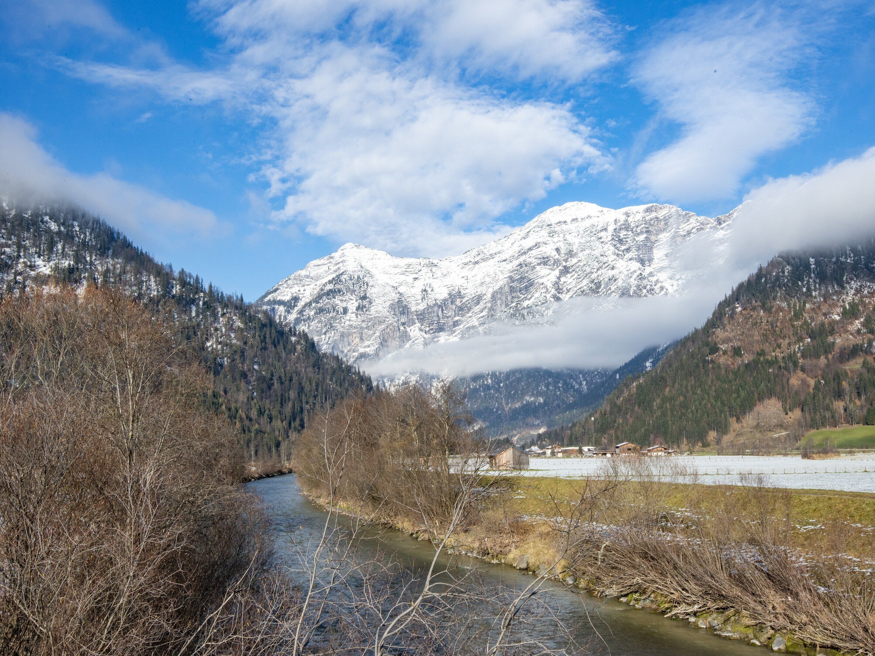 A river flowing through a valley with snow-capped mountains in the background.