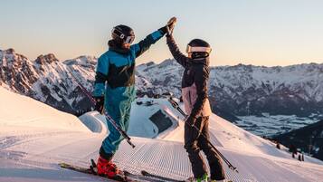 Deux skieurs se donnent la main en signe de camaraderie sur une pente enneigée, avec une montagne en arrière-plan.