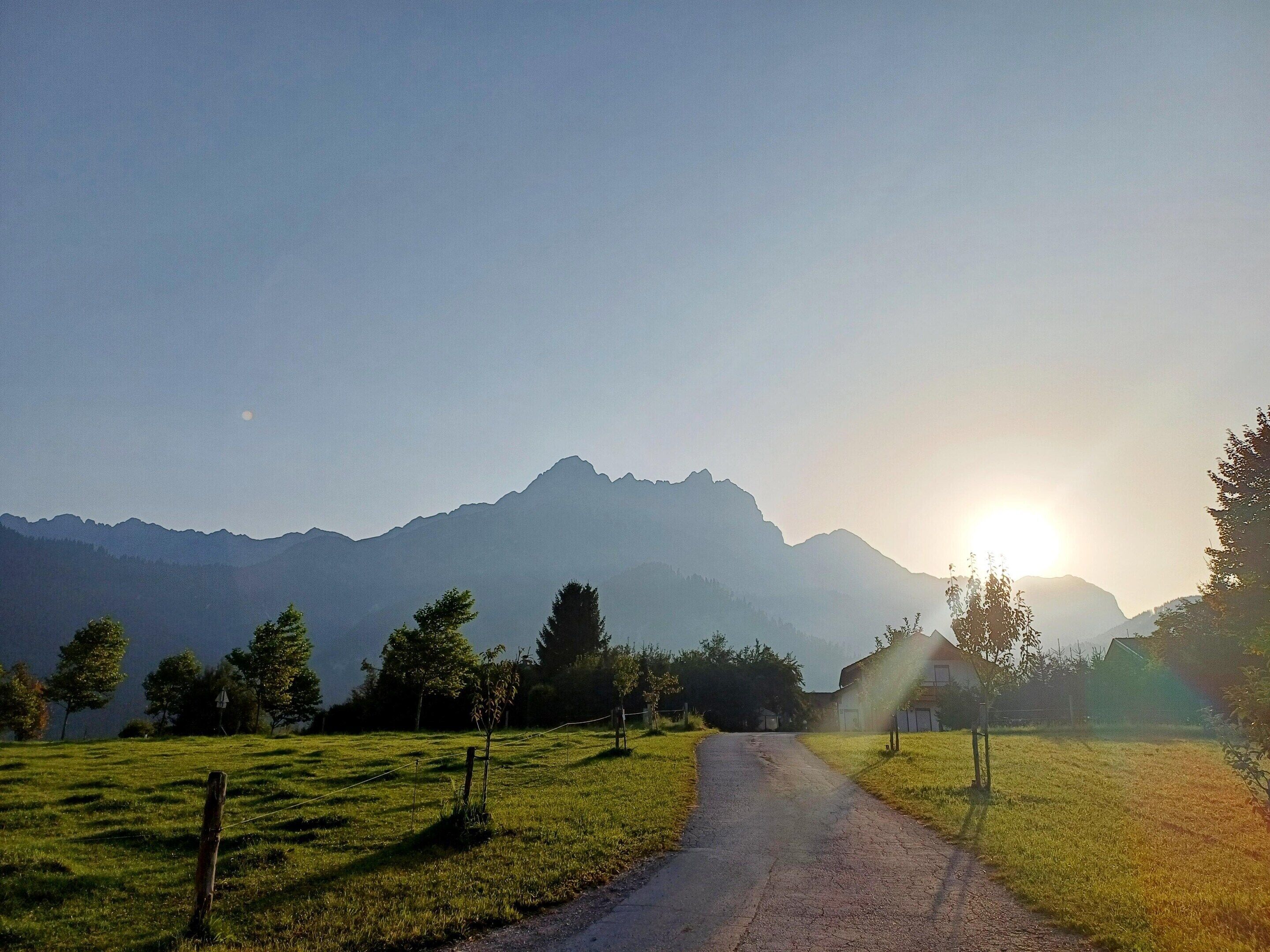Un camino rural que atraviesa un campo cubierto de hierba, con montañas al fondo.