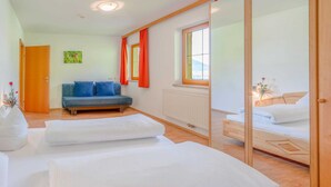 A modern hotel room with a large bed, a sofa, a window with curtains, and a view of the outdoors. - Apartment in Stubaital Near Ski Lift (Neustift Im Stubaital)