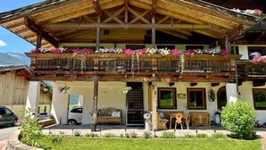 A two-story wooden building with balconies adorned with flowers, a bench, and a small garden area. - Apartment in Saalfelden am Steinernen Meer (Saalfelden am Steinernen Meer)