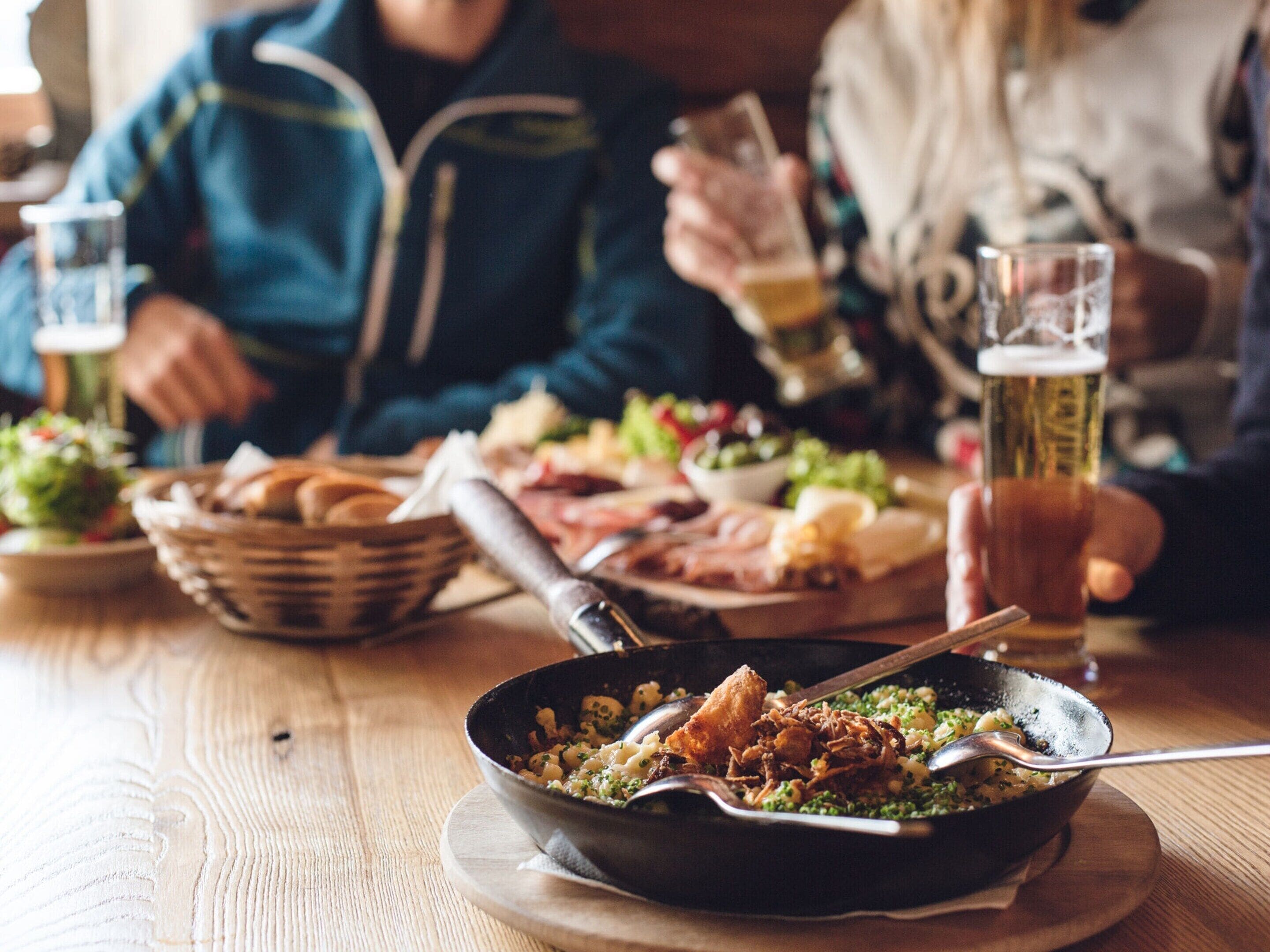 A dining table with various dishes, including a bowl of food, a basket of bread, and a glass of beer.