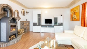 Un salon moderne avec une cheminée en pierre, une table basse en verre, un canapé blanc et un téléviseur à écran plat.